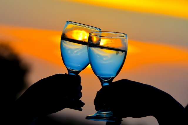 海辺のレストランで乾杯をするカップルの手元と夕焼け